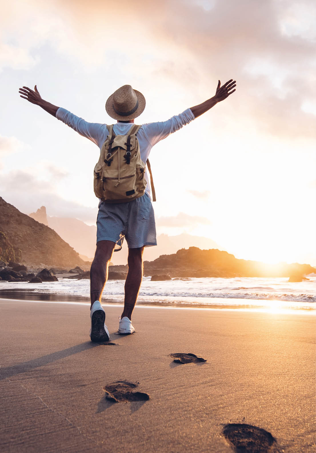 Young man arms outstretched by the sea at sunrise enjoying freedom and life, people travel wellbeing concept