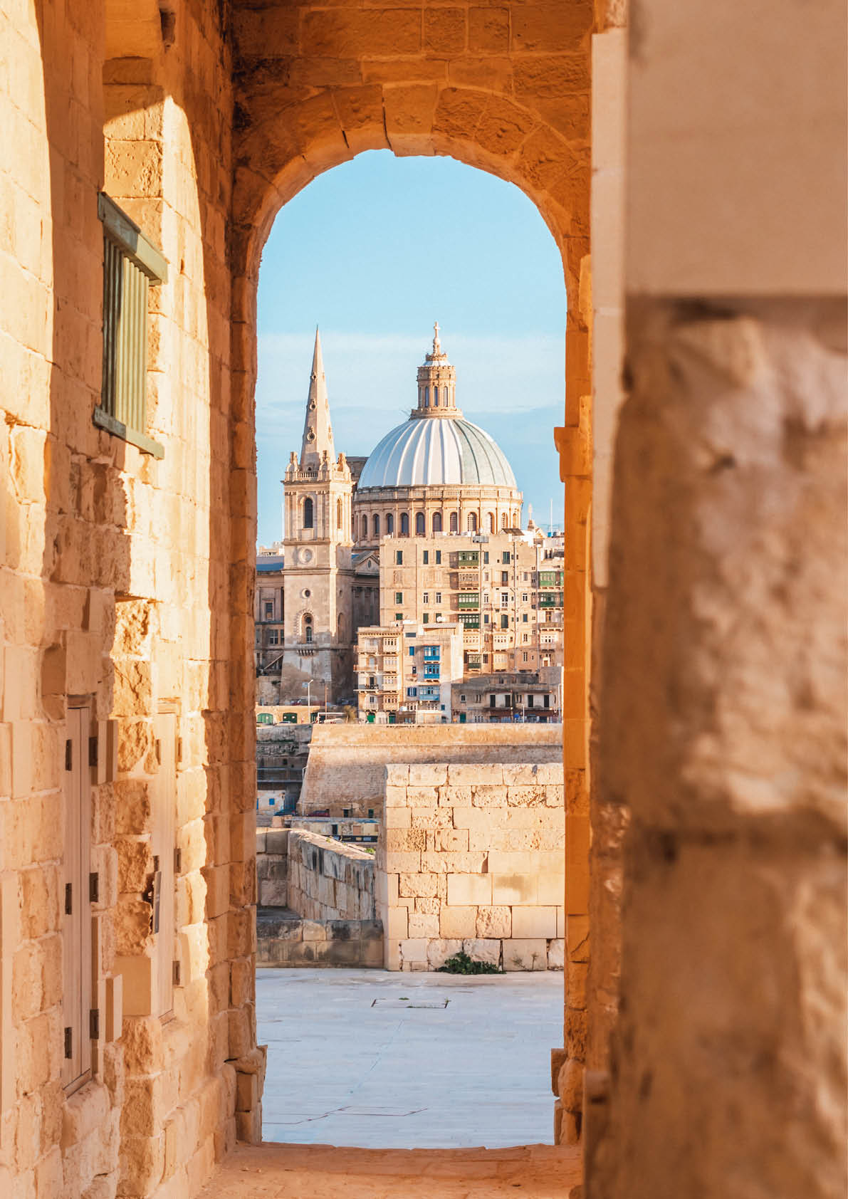 Blick durch einen Steinbogen auf die Kuppel und den Turm zweier Kirchen in Valletta.
