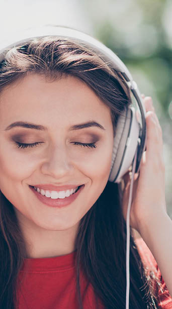 Close up portrait of young brunette girl closes her eyes from pleasure listening to music and holding headphones by hand