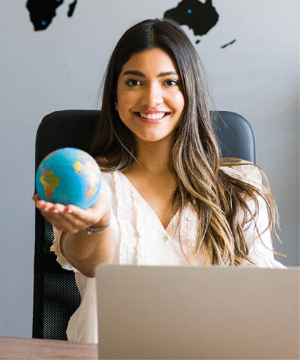 Holding the world in my hands. Attractive female travel agent showing a globe and smiling while working at her modern office