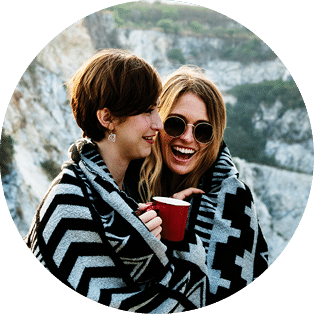 Girlfriends cuddle together under blanket on top of the mountain