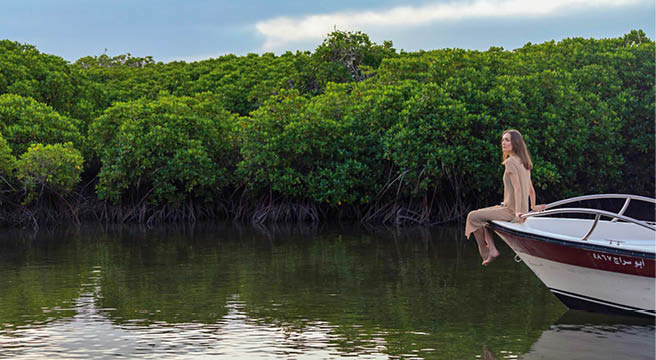 A view of a young woman sitting on the bow of a boat cruising through the mangrove forest of the Farasan Islands