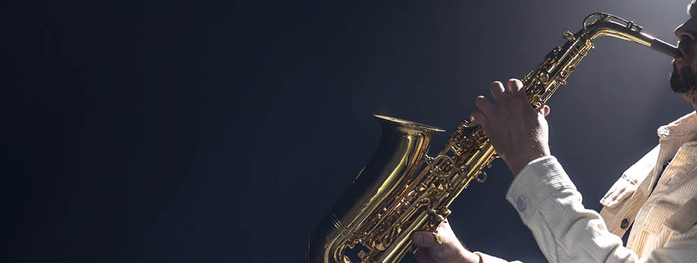 A young man plays the saxophone. Saxophonist on a dark background. Space for text. High quality photo. Musician on a black background. Copy space.