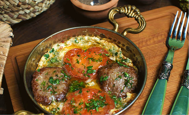 a front close up view cooked eggs along with red tomatoes inside metallic pan on the brown wooden desk
