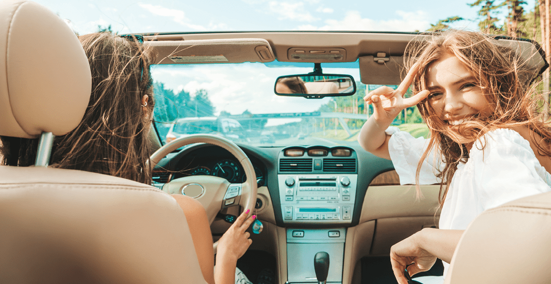 Portrait of two young beautiful and smiling hipster female in convertible car. Sexy carefree women driving cabriolet. Positive models riding and having fun in sunglasses outdoors.Enjoying summer days