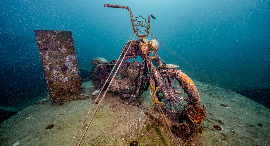 Underwater scene of submerged rusty motorcycle for artificial coral reef at Tor 13 dive site or the underwater museum in Andaman sea, Thailand.