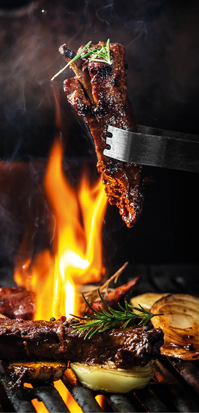 Grilled pork ribs on the grill chopped on a fork against a fire. The cook holds a fork in his hand. concept cooking meat. Close up. place for text.