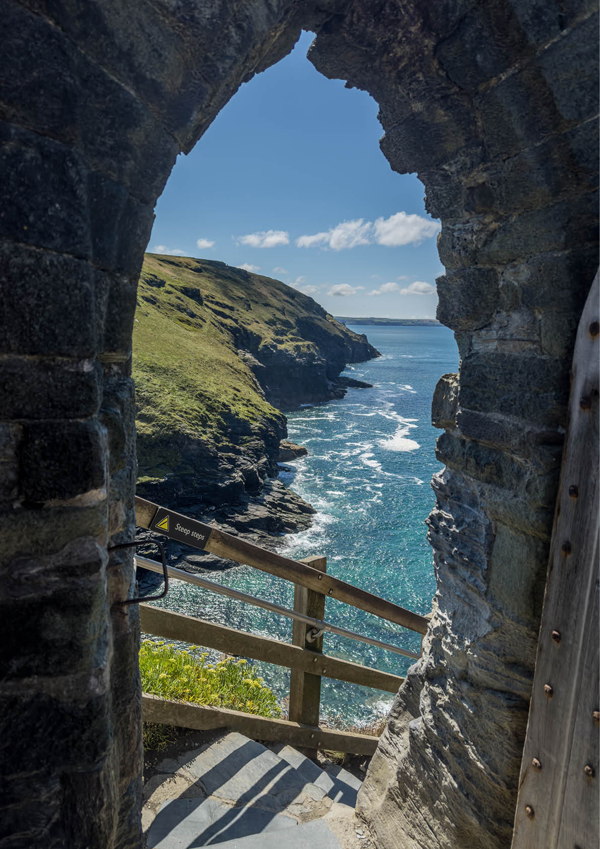 Blick durch steinernen Torbogen auf K ste und Meer mit Treppe im Vordergrund