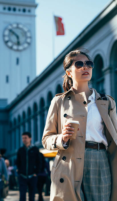 Frau mit Sonnenbrille und Becher vor Geb ude mit Uhrturm