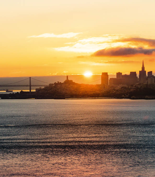 Skyline bei Sonnenuntergang mit Br cke und Wasser im Vordergrund