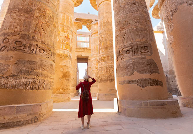 Woman traveler explores the ruins of the ancient Karnak temple in the city of Luxor in Egypt. Great row of columns with carved hieroglyph