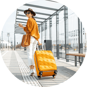 Young female traveler walking with a yellow suitcase at the modern transport stop outdoors, back view. Concept of an urban transportation and travel
