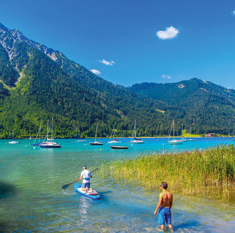 Man on surfing board sailing on beautiful Achensee lake on sunny summer day, Tirol, Austria