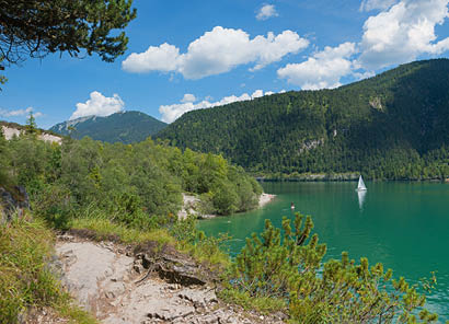 Idyllischer Uferweg am Achensee entlang, blaugr nes Wasser mit Segelbooten. Sommertag mit blauem Himmel und Wolken.