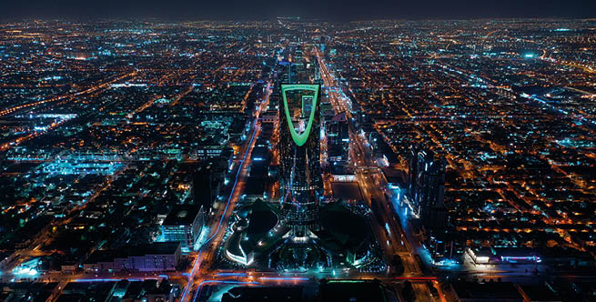 A dramatic aerial view of Riyadh at night, with the illuminated Kingdom Tower in the center