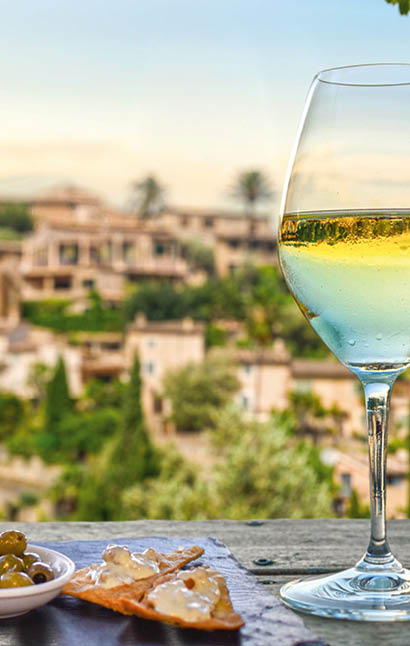 A glass of white wine with appetizers in front of a Mediterranean background