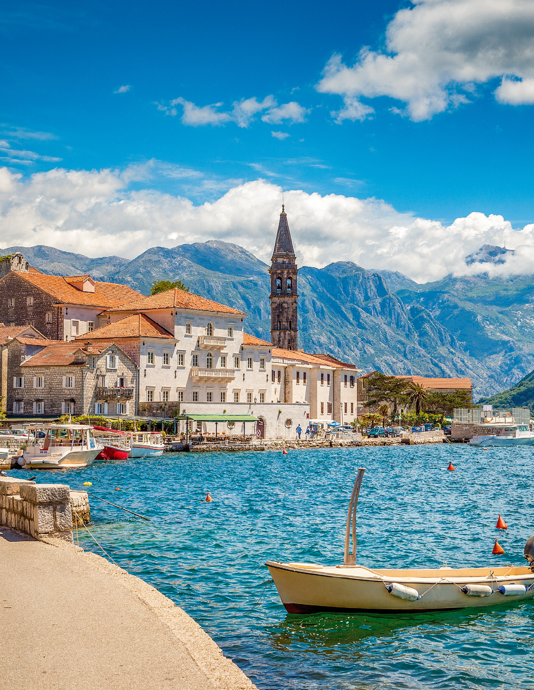 Scenic panorama view of the historic town of Perast at famous Bay of Kotor with blooming flowers on a beautiful sunny day with blue sky and clouds in summer, Montenegro, southern Europe