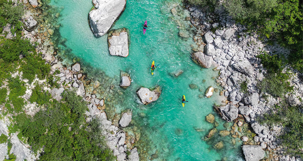 Aerial drone view of three kayaks on the turquoise Soca river. Idyllic top view of clear water, rocks and trees. Kayaking in Slovenia