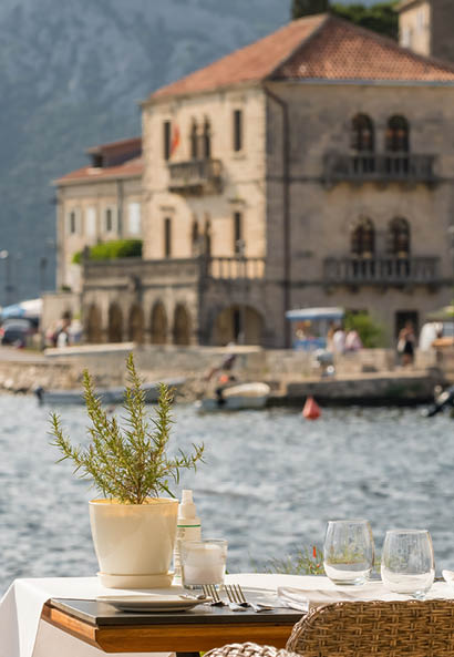 Street view of a outdoor waterfront terrace with tables and chairs in restaurant in Perast historic village in Kotor Bay, Montenegro. Summer vacation destination concept