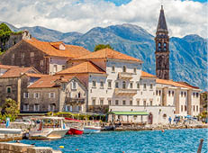 Scenic panorama view of the historic town of Perast at famous Bay of Kotor with blooming flowers on a beautiful sunny day with blue sky and clouds in summer, Montenegro, southern Europe