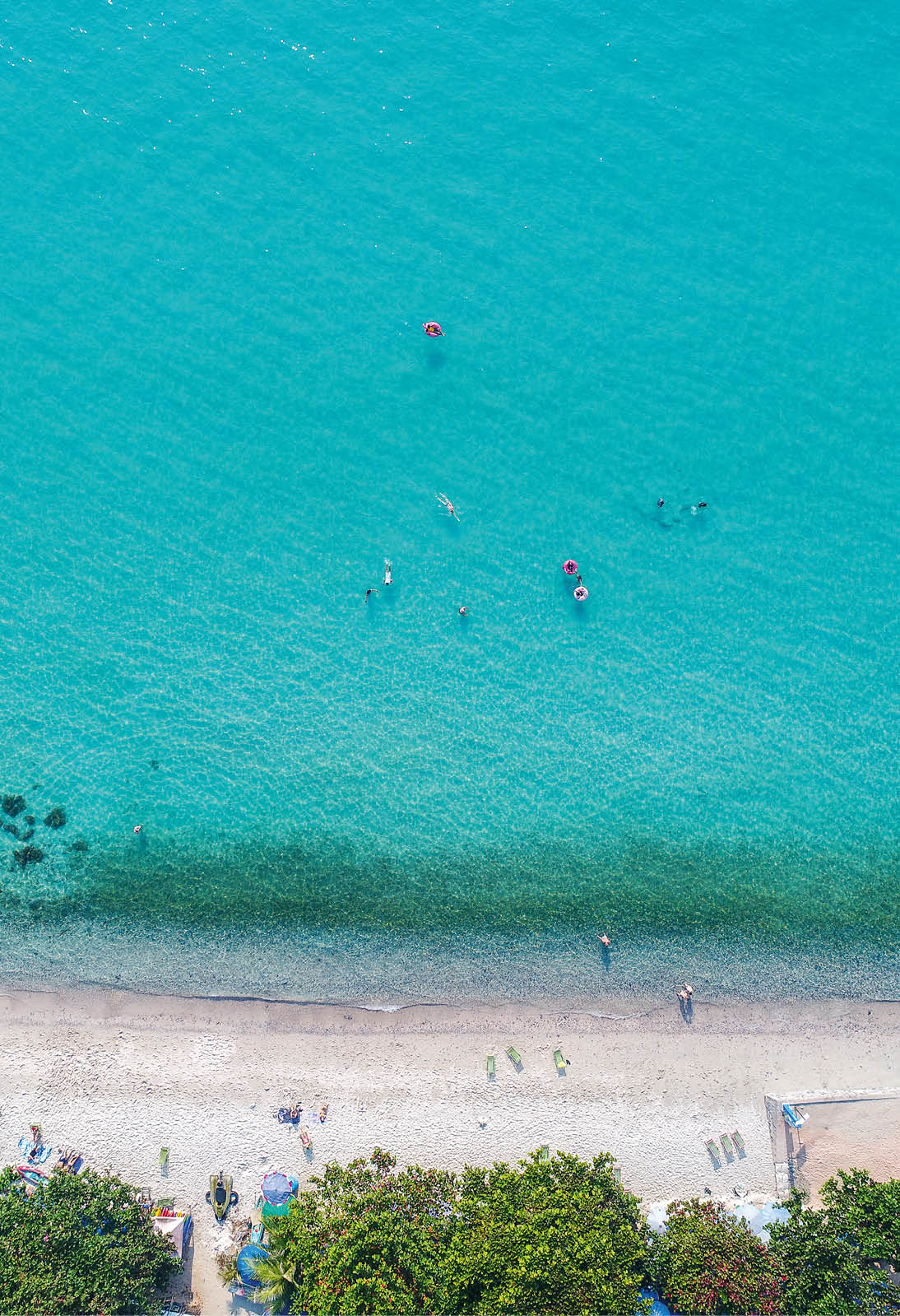 Aerial view of sandy beach with tourists swimming.
