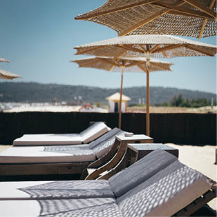 A selective vertical shot of white loungers under parasols by the beach
