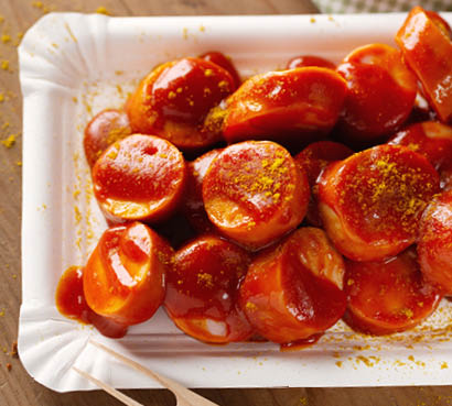 Spicy tasty appetizing cut currywurst with ketchup served on plate. Closeup. 