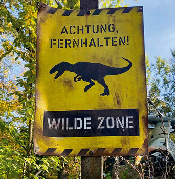 Gelbes Schild mit der Aufschrift „Achtung, fernhalten! Wilde Zone“ und Dinosauriersymbol.