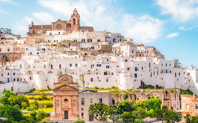 Dicht gebaute wei e H user mit Kirche auf H gel unter blauem Himmel, typisch s ditalienisch.