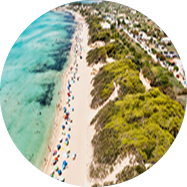 Luftaufnahme eines Sandstrandes mit Badeg sten und vielen bunten Sonnenschirmen am klaren Wasser.