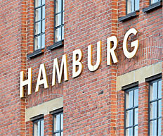 Gro e gelbe Buchstaben „HAMBURG“ an roter Backsteinfassade mit Fenstern.