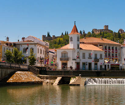 Stadt Tomar, Portugal: H user mit roten D chern an Fluss mit Wehr, dahinter Burganlage auf H gel.