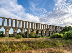 Langes Stein-Aqu dukt mit doppelter Bogenreihe ber Wiese unter teils bew lktem Himmel.