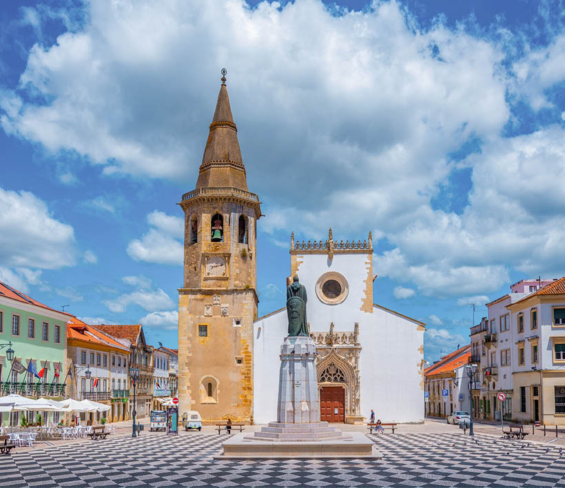 Kirche Sao Joao Batista in Tomar, Portugal: Platz mit gepflastertem Schachbrettmuster, gotischer Kirche, Glockenturm und Denkmal.