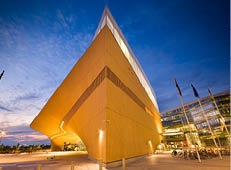 Zentralbibliothek Oodi in Helsinki: Gro es, futuristisches Bauwerk mit beleuchteter Holzfassade neben Glasgeb ude bei Abendhimmel.