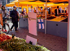 Frischer Gem sestand mit Erbsen, finnischer Flagge und Verkaufsst nden unter orangen Zelten.
