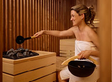 Eine gl ckliche Frau gie t Wasser auf hei e Steine in der Sauna.