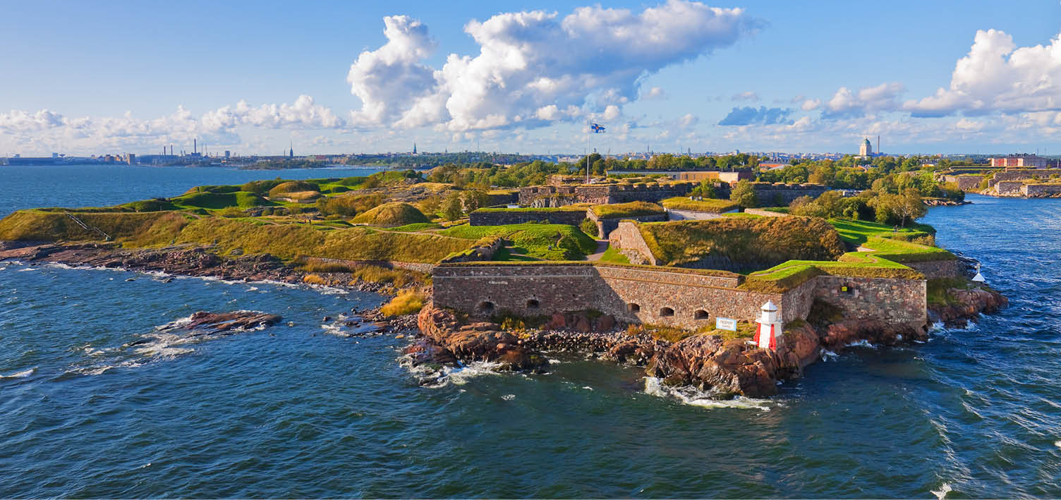 Festung Suomenlinna in Helsinki. Alte Befestigungsanlage mit Leuchtturm auf gr ner Insel im Meer, Stadt am Horizont sichtbar.
