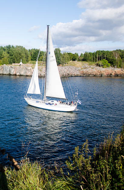 Wei es Segelboot f hrt bei leichtem Wind vor einer bewaldeten Felsk ste.