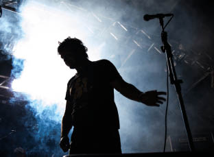 Silhouette eines Mannes vor Mikrofon auf B hnenpodest mit Nebel und starkem Gegenlicht.