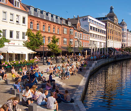 Aarhus, D nemark: Zahlreiche Menschen sitzen und spazieren an einer Promenade vor Restaurants und historischen Fassaden.