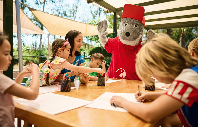Bild von TUI-Roby-Club mit Kindern, die am Tische malen. Im Hintergrund das Maskottchen vom Roby-Club