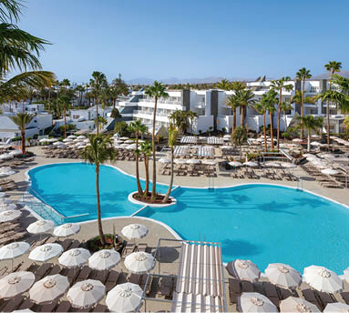 Gro e Poollandschaft mit Sonnenliegen und Palmen in moderner Hotelanlage bei klarem Himmel.