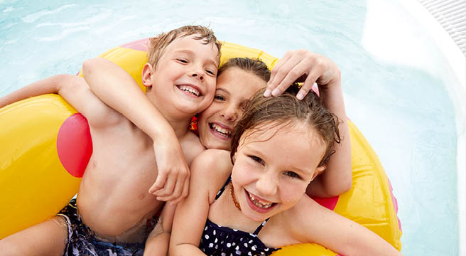 Mutter mit zwei Kindern sitzt im Schwimmring im Pool