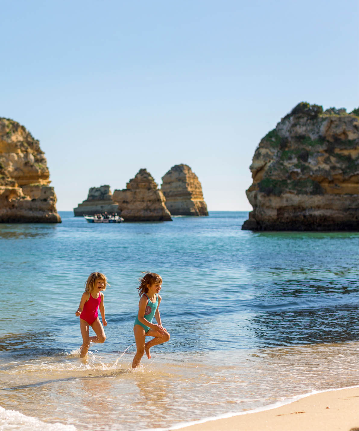 Zwei M dchen in Badeanz gen laufen im seichten Wasser vor markanten K stenfelsen.