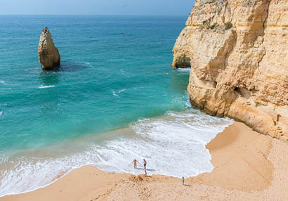 Heller Sandstrand mit Felsen, t rkisfarbenem Wasser und wenigen Menschen im Uferbereich.
