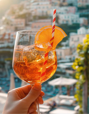 Hand h lt Glas mit orangefarbenem Cocktail und Strohhalm vor verschwommener K stenstadt.