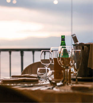 Gedeckter Tisch mit Gl sern und Flasche vor Glasbalustrade mit Blick auf Meer und Berge.