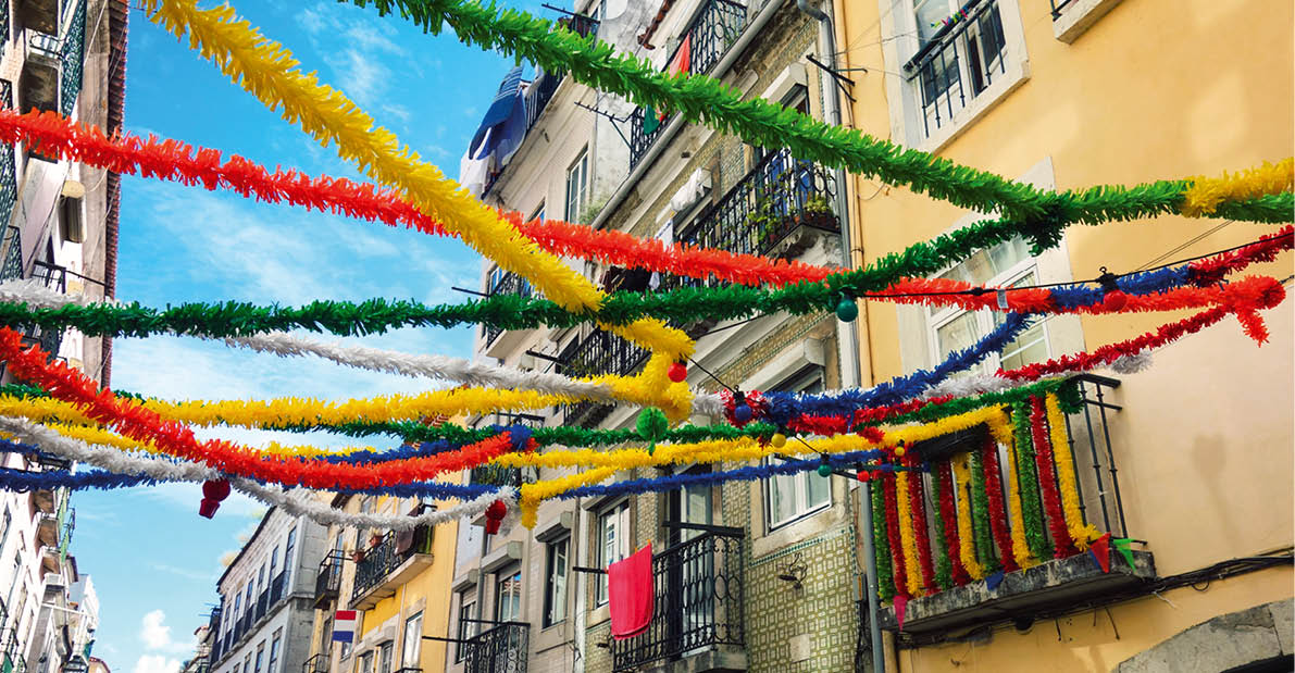 Mehrfarbige Girlanden h ngen zwischen Balkonen einer Altstadtgasse bei blauem Himmel.
