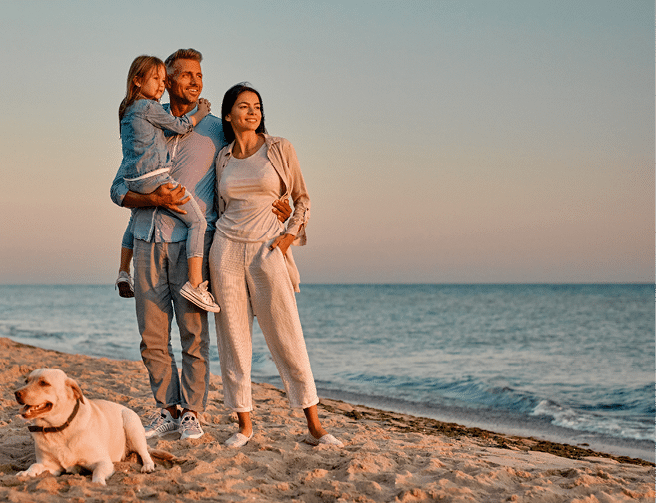 Happy family concept. Young attractive mother, handsome father and their little cute daughter standing together on the beach with dog.